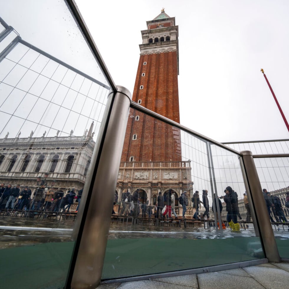 Turistas y vecinos caminan sobre pasarelas durante una marea de 97 centímetros para cruzar la inundada Plaza de San Marcos, Venecia, 10 de diciembre de 2022.