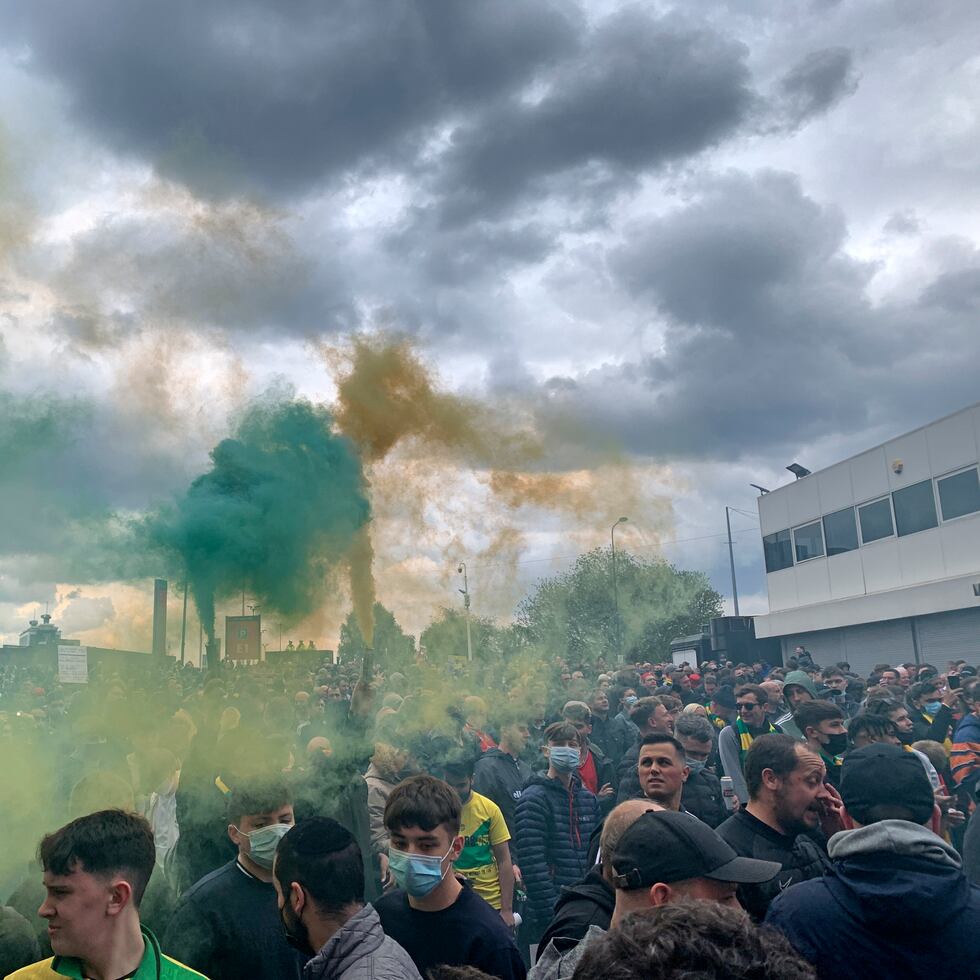 Los fanáticos del Manchester United sostienen bengalas mientras protestan afuera de Old Trafford.