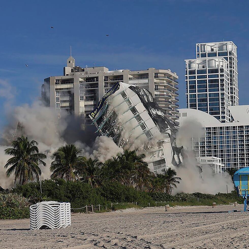 La torre del hotel de 17 pisos del histórico Deauville Beach Resort en Miami Beach implosiona y envía polvo lleno de escombros a los edificios de lujo junto al mar.