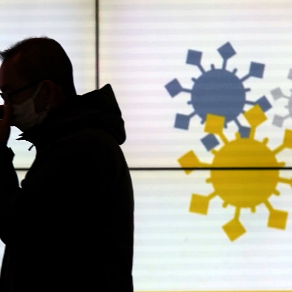 A man wearing a protective mask to help curb the spread of the coronavirus walks in front of a public awareness notice on the omicron coronavirus variant Thursday, Jan. 13, 2022, in Tokyo. (AP Photo/Eugene Hoshiko)