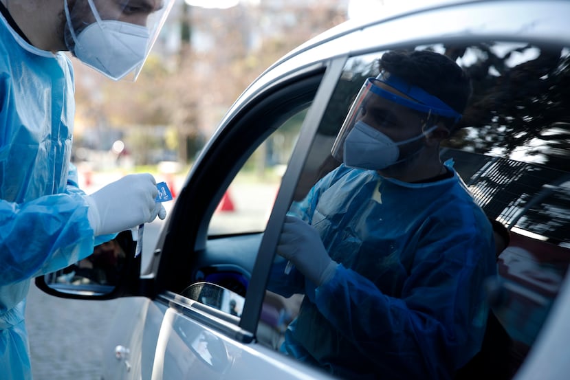 Un miembro del personal médico de la Organización Nacional de la Salud (EODY) se prepara para realizar una prueba rápida de COVID-19 en una mujer en un sitio de pruebas de tránsito en Atenas.