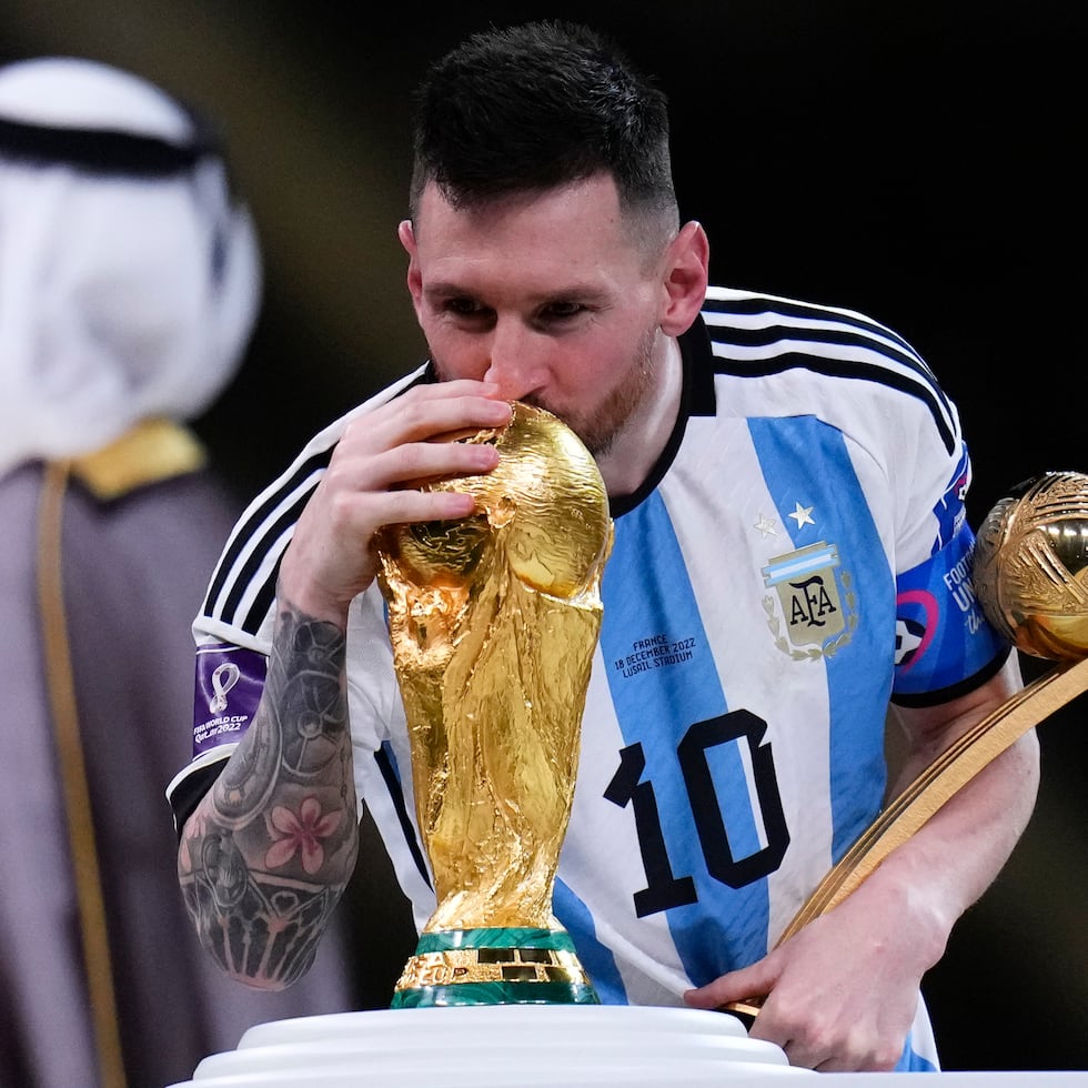 Lionel Messi besa el trofeo de la Copa del Mundo mientras sostiene el premio al mejor jugador del torneo.