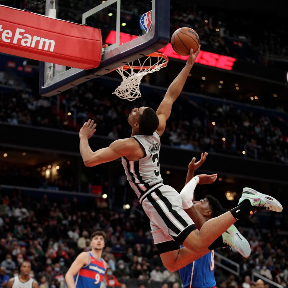 Keldon Johnson (3), de los Spurs de San Antonio, se contorsiona para intentar anotar al tiempo que recibió una falta de Rui Hachimura, de los Wizards de Washington.