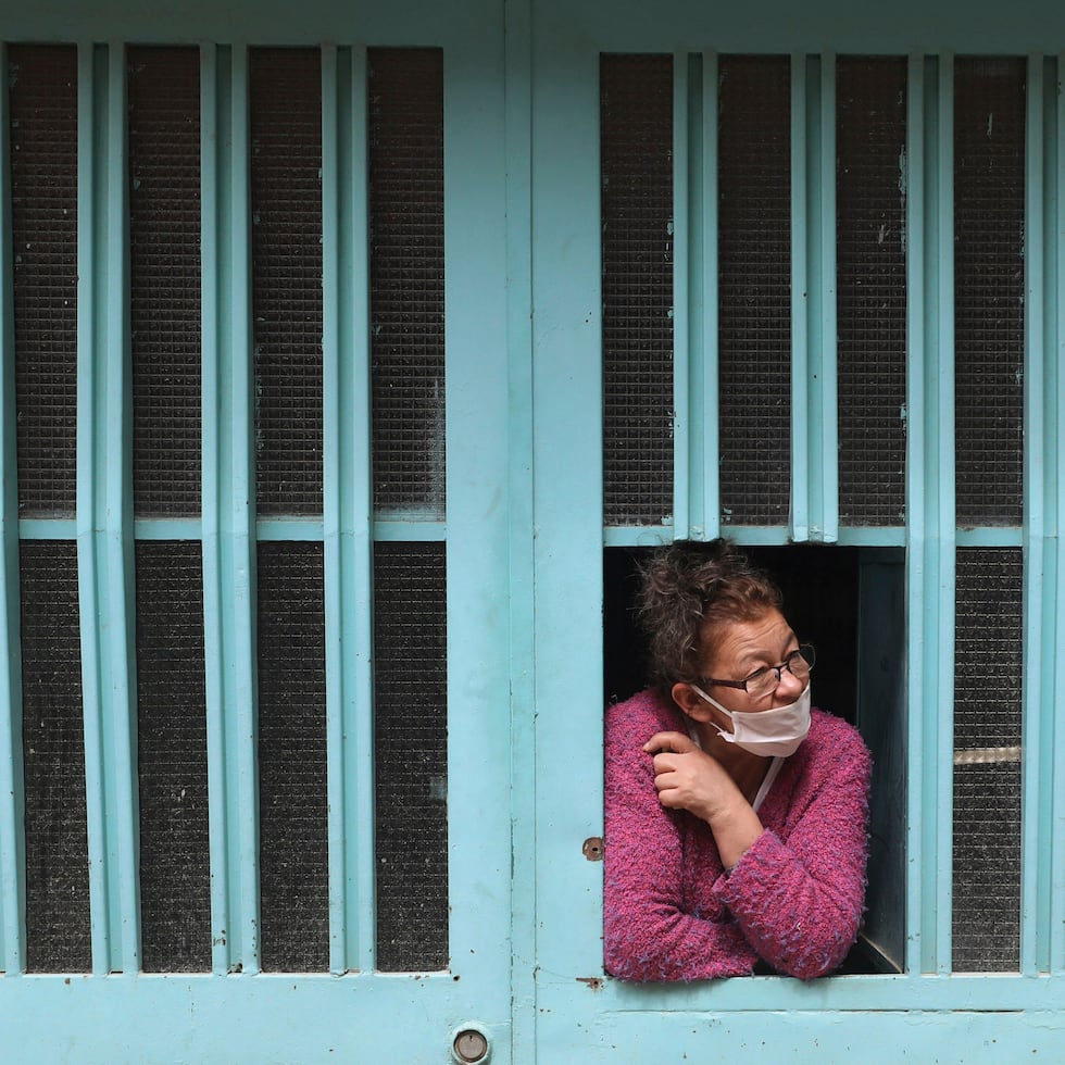 Una mujer observa desde la ventana de su casa mientras espera recibir comida gratis del gobierno de la ciudad el viernes 12 de junio de 2020, en Bogotá, Colombia, donde continúan las medidas de prevención por el coronavirus. (AP Foto/Fernando Vergara)