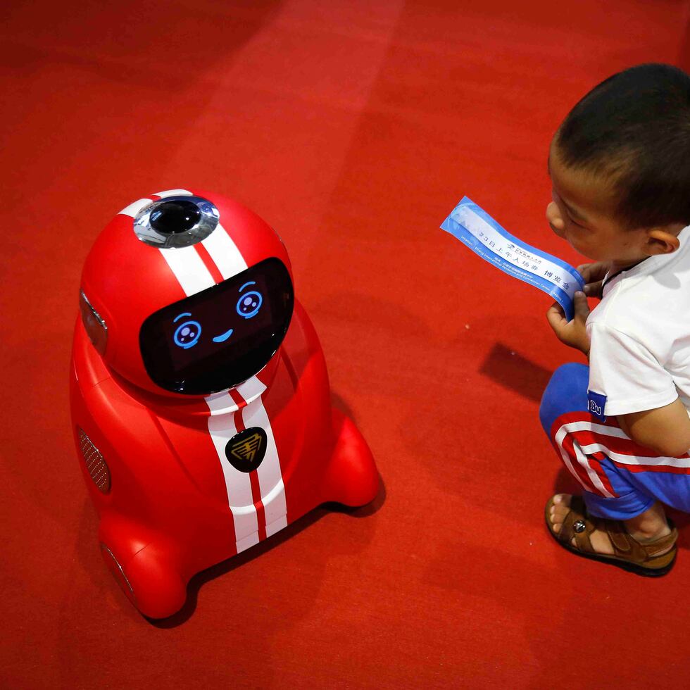 Un niñito sostiene una entrada al Congreso Mundial de Robots mientras observa a un robot con capacidad de autoaprendizaje. AP