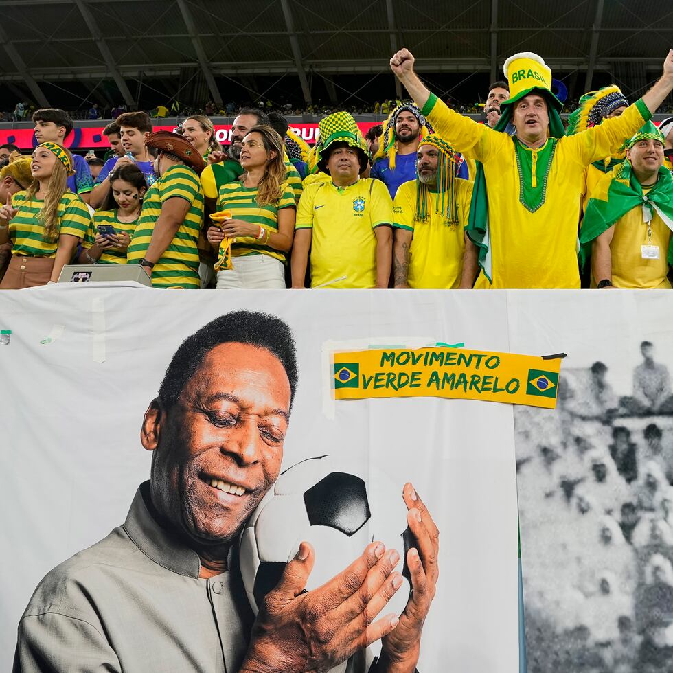 Aficionados de Brasil alientan a la selección detrás de un cartel con imágenes de Pelé, el lunes 5 de diciembre de 2022, antes de un partido del Mundial ante Corea del Sur en Al Rayán, Qatar (AP Foto/Martin Meissner)
