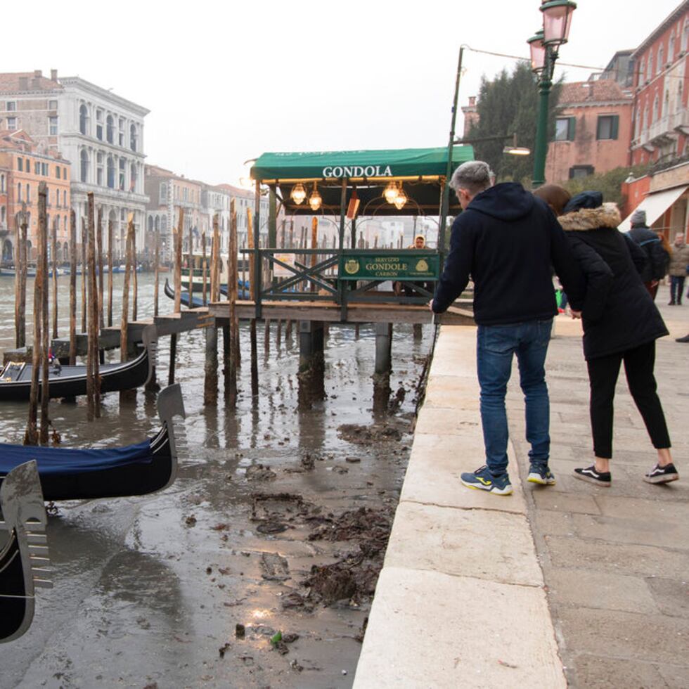 Varias personas observan las góndolas atracadas en un canal durante la marea baja en Venecia, Italia, el martes 21 de febrero de 2023. (AP Foto/Luigi Costantini)