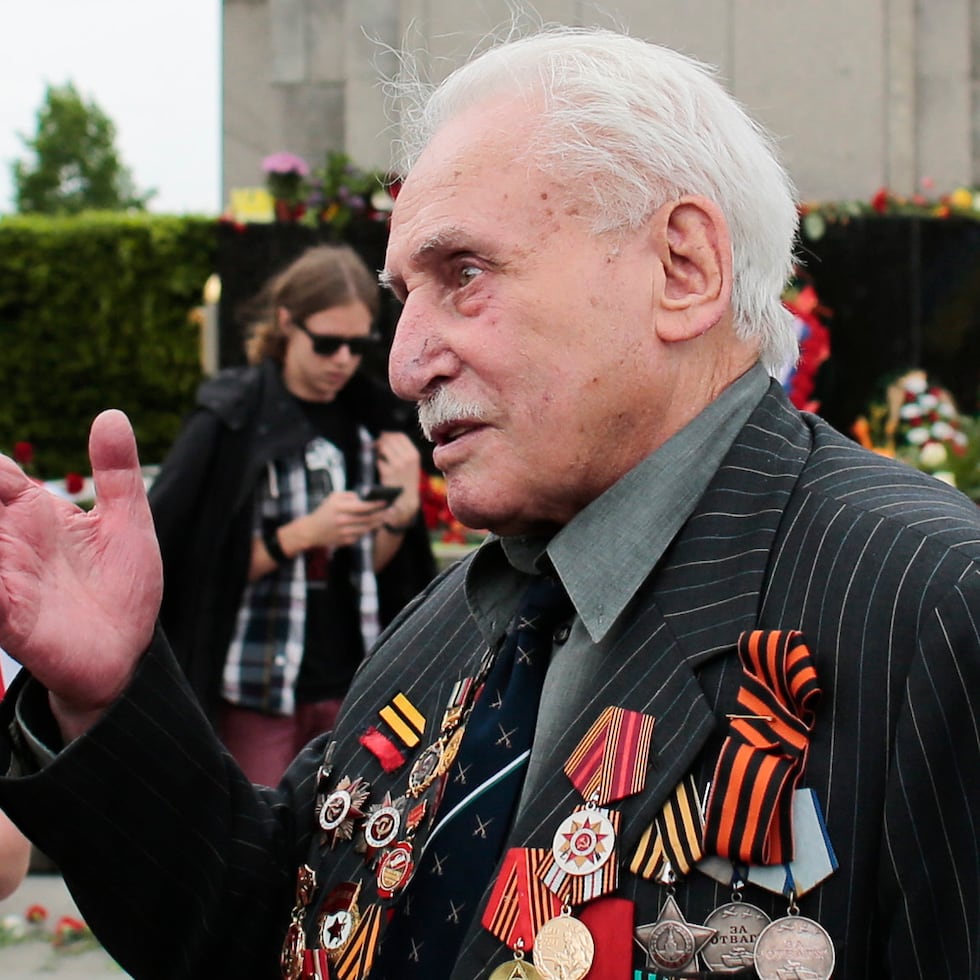 En esta imagen del viernes 8 de mayo de 2015, David Dushman, de 92 años, veterano de guerra de la ex Unión Soviética, habla con personas que ondean banderas ucranianas durante una ceremonia en el Monumento de Guerra Soviético en el Tiergarten, en Berlín, Alemania.