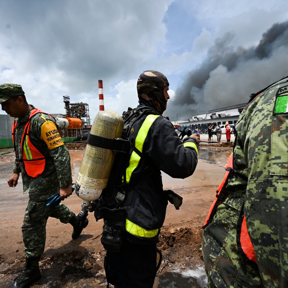 A Cuban firefighter stands between Mexican soldiers as they work to put out a deadly fire at a large oil storage facility in Matanzas, Cuba, Tuesday, Aug. 9, 2022. The fire was triggered when lighting struck one of the facility's eight tanks late Friday, Aug. 5th. (Yamil Lage, Pool photo via AP)