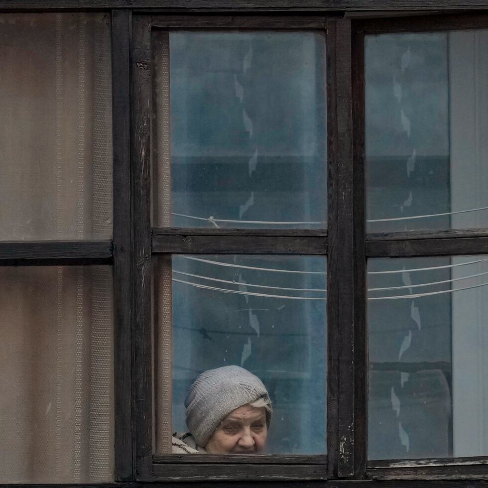 Una mujer mira por la ventana de una vivienda en Sievierodonetsk, en la región de Luhansk, en el este de Ucrania, el 18 de febrero de 2022. (AP Foto/Vadim Ghirda)