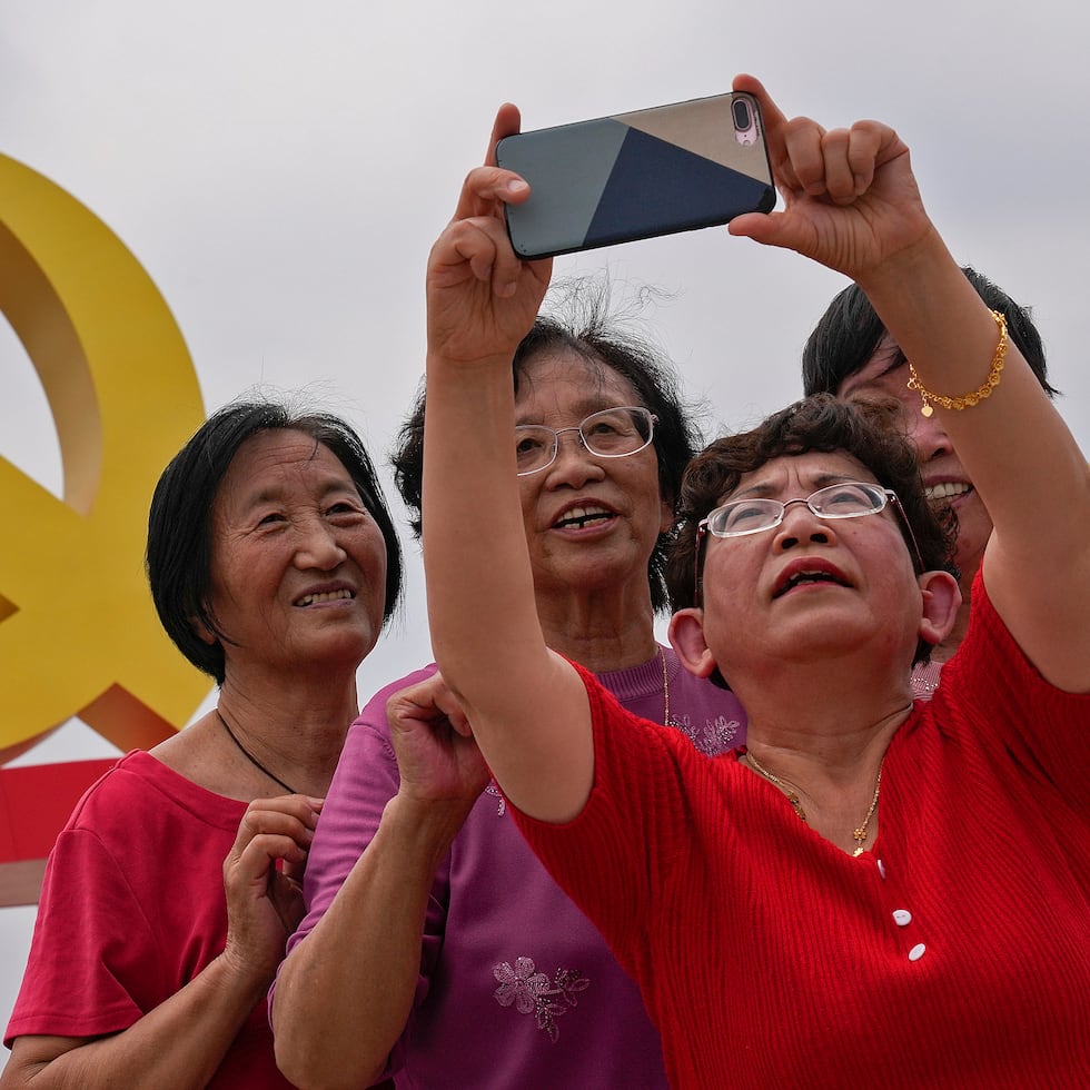 Women take a selfie with a communist party's logo on display at Tiananmen Square to mark the 100th anniversary of the founding of the ruling Chinese Communist Party in Beijing on Monday, July 5, 2021. Chinese leader Xi Jinping on Tuesday attacked calls from some in the U.S. and its allies to limit their dependency on Chinese suppliers and block the sharing of technologies. (AP Photo/Andy Wong)