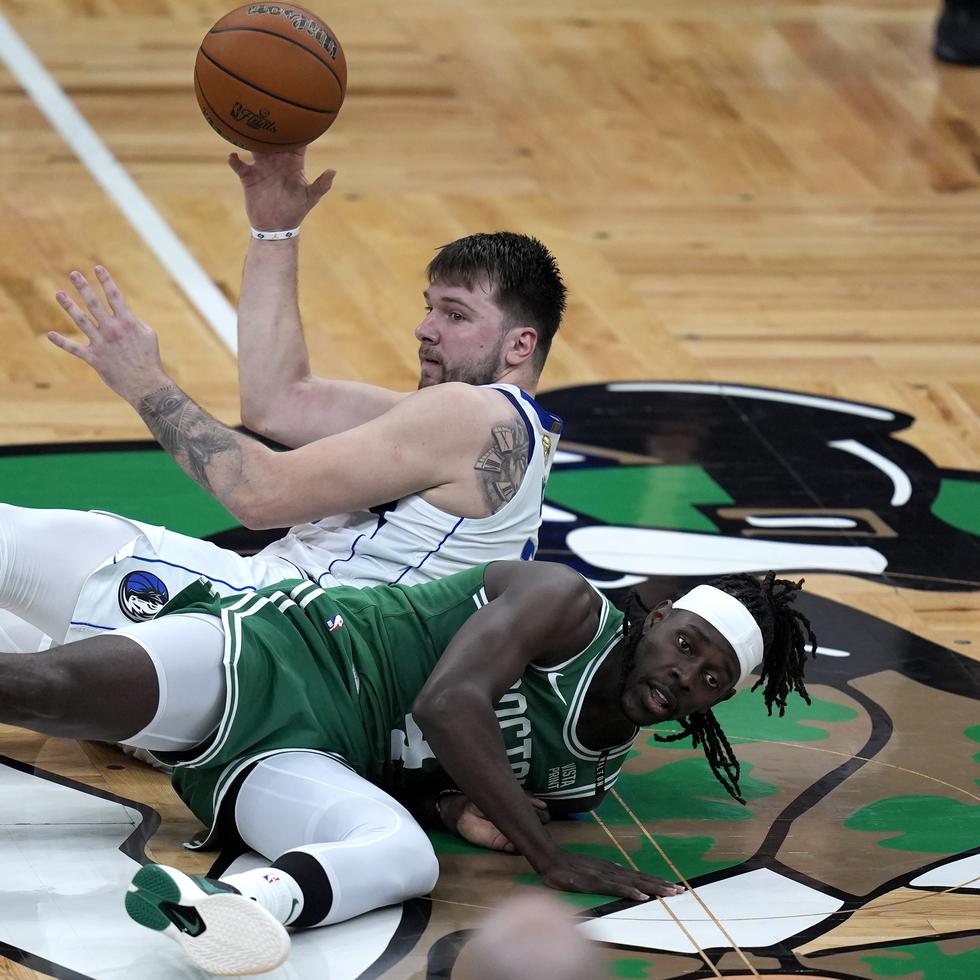 Luka Doncic, de los Mavericks, buscando a quién pasarle el balón tras caer al suelo, junto a Jrue Holiday, de los Celtics de Boston.