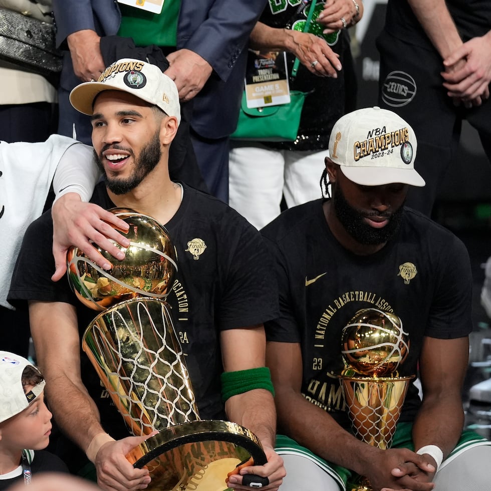 Jayson Tatum, al centro con el trofeo de campeonato Larry O'Brien, y Jaylen Brown a la derecha con el premio de Jugador Más Valioso, durante la celebración de los Celtics la noche del lunes.
