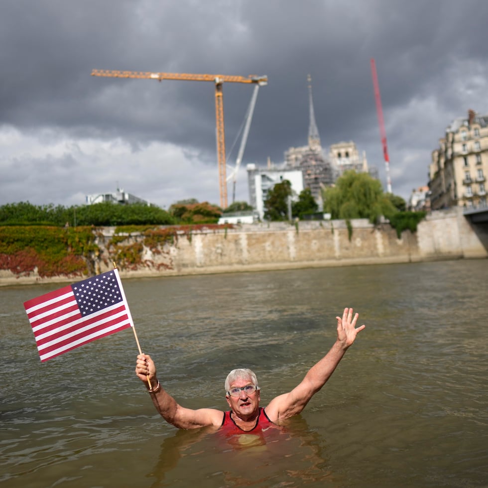 Joel Stratte-McClure, de los Estados Unidos, sostiene una bandera luego de completar un corto nado en el Río Sena, el jueves 4 de julio, en París.